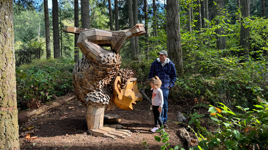 father and daughter looking at a Thomas Dambo troll doing a handstand at NW Trek in Washington