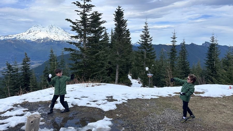 two children having a snowball fight near their MTTA hut, with snow-covered Mount Rainier in the background