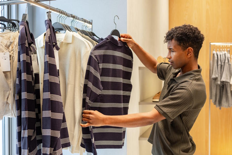 Teenage boy holding up a shirt in a store shopping for clothes