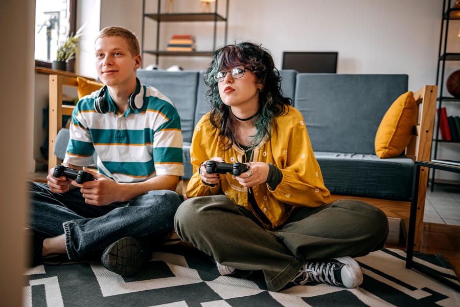 Two teenage friends playiung video gmaes togehter in their living room