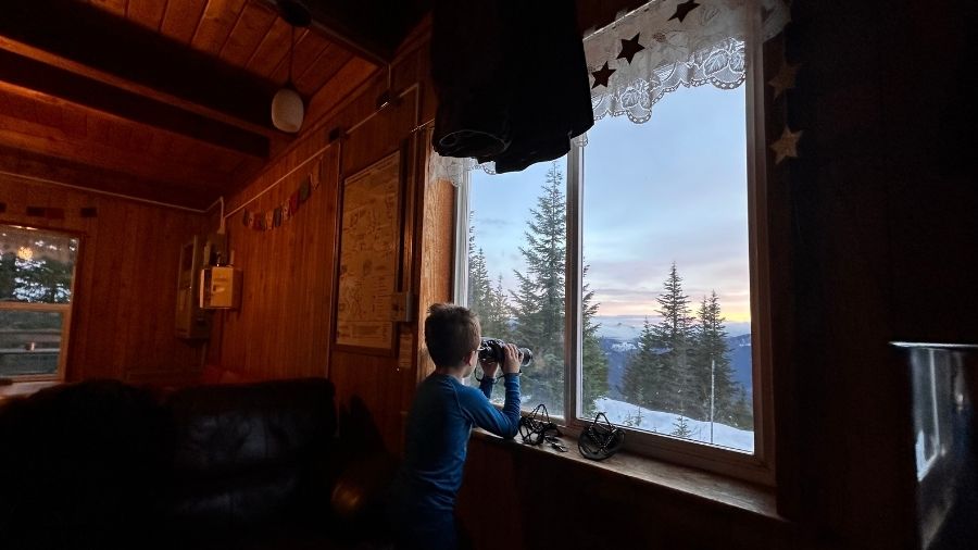 child looking through binoculars at snowy mountain views from inside a Mount Tahoma Trails Association hut