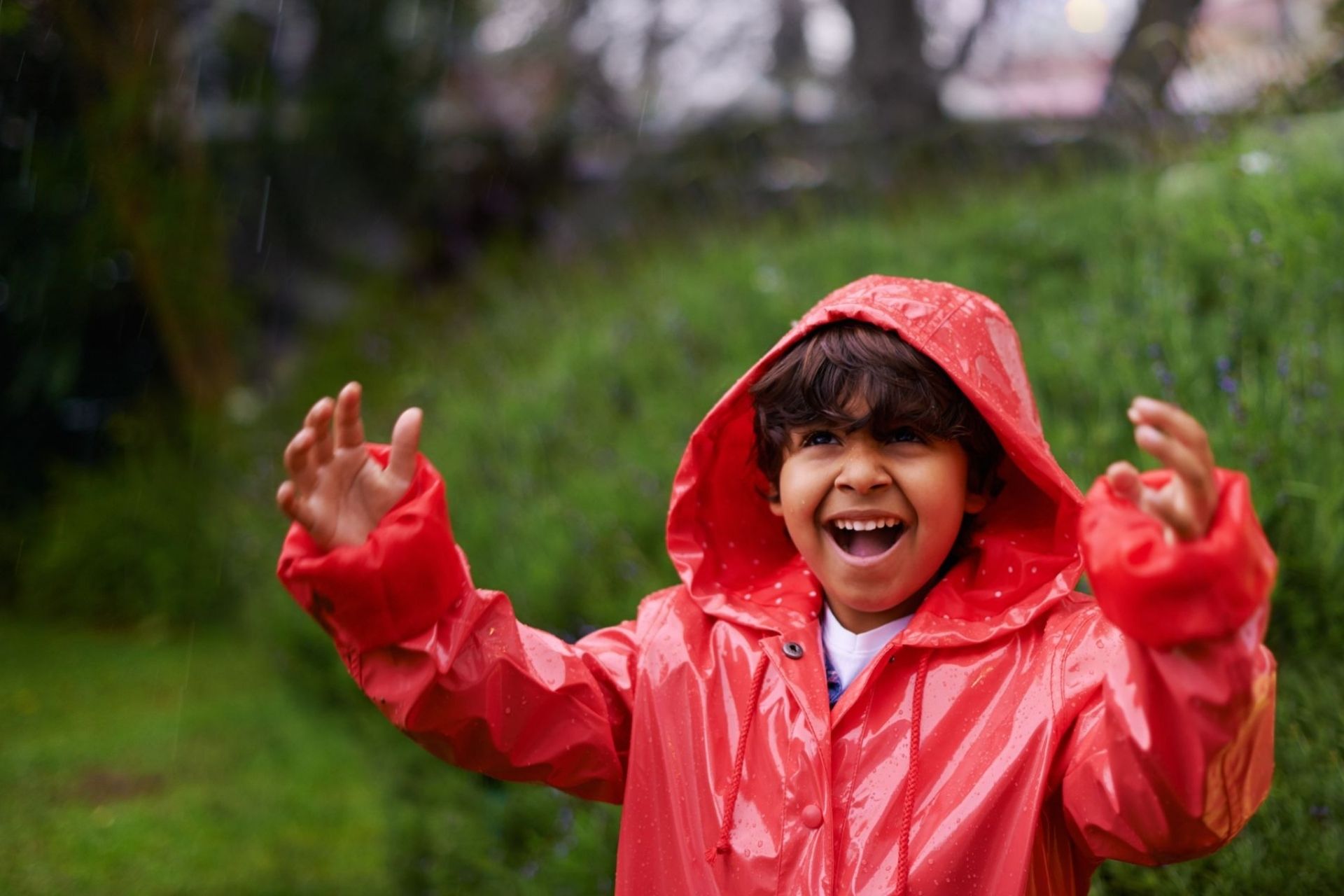 little boy happy in the rain wearing red raincoat