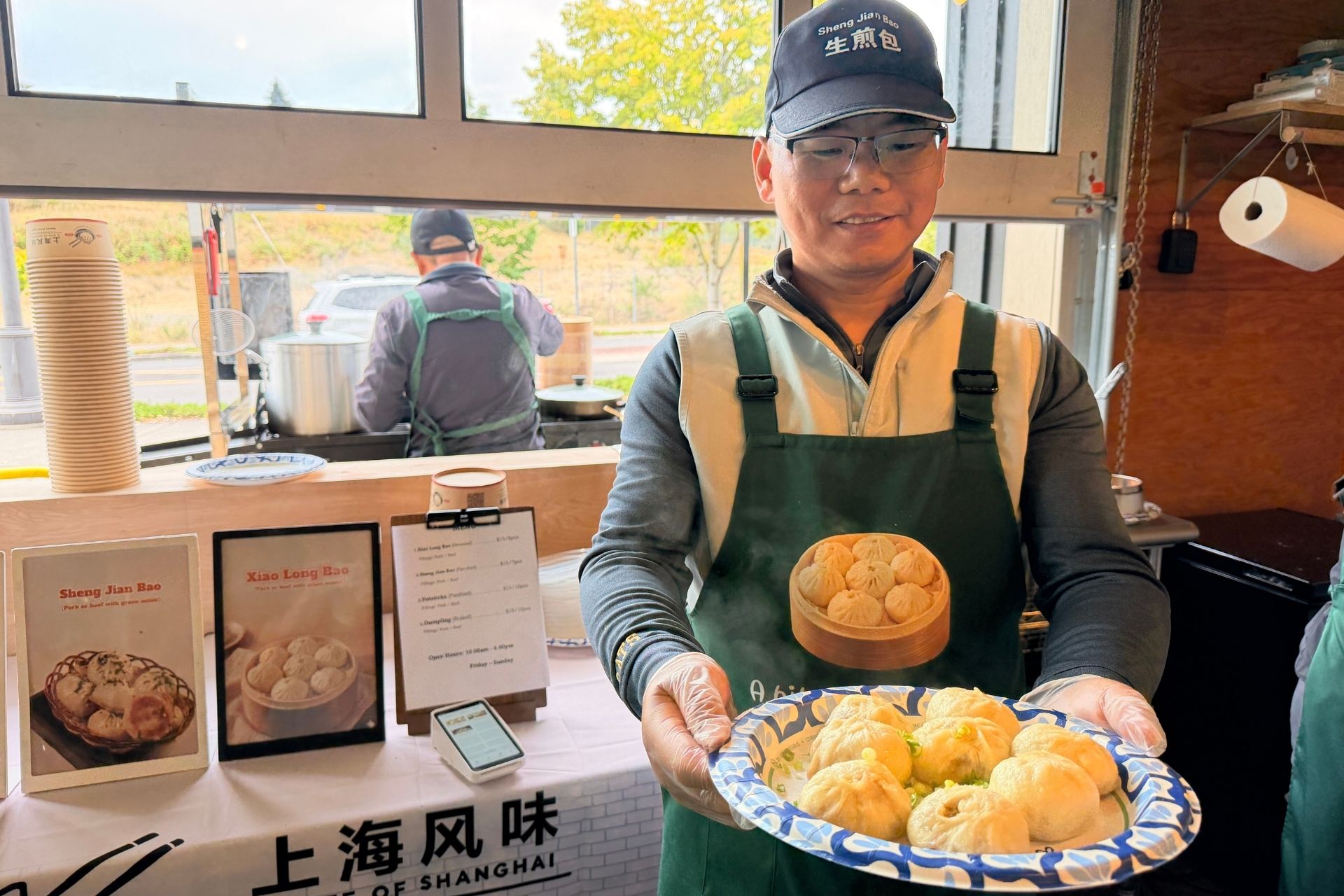 a worker at a bite of shanghai in tacoma holding a plate of freshly steamed chinese soup dumplings, or xiao long bao